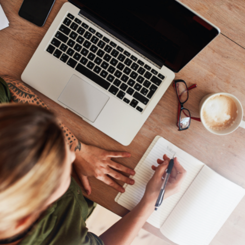 Woman writing in a notebook next to laptop and coffee